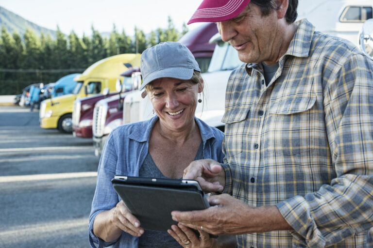 Caucasian woman and man truck driving team working on their driving log in a truck stop parking lot.